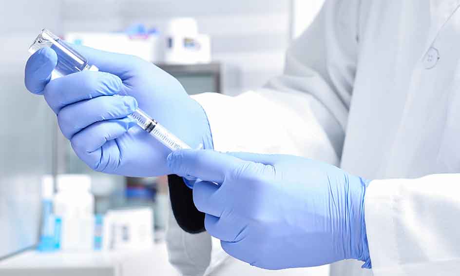 Close-up on man hands , wearing protective gloves, dialing medicine into syringe from a vaccine vial