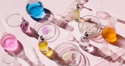Colorful background with laboratory utensils, samples of cosmetics and glass vials on pink background.